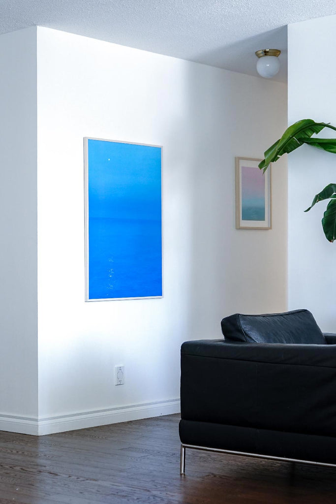 Two seascape oil paintings on a white wall in a minimalism home. Painting on the left is bright blue, on the left is pink and green.