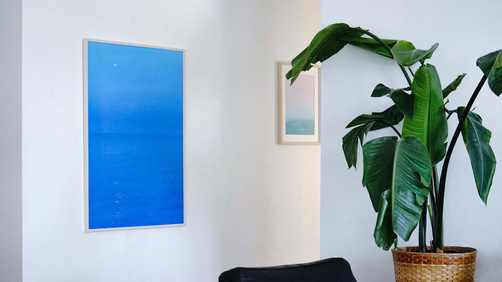 Two seascape oil paintings on a white wall in a minimalism home. Painting on the left is bright blue, on the left is pink and green.